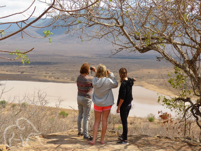 drie vrouwen op een heuvel kijkend en wijzend over Mkomazi landschap met een meertje