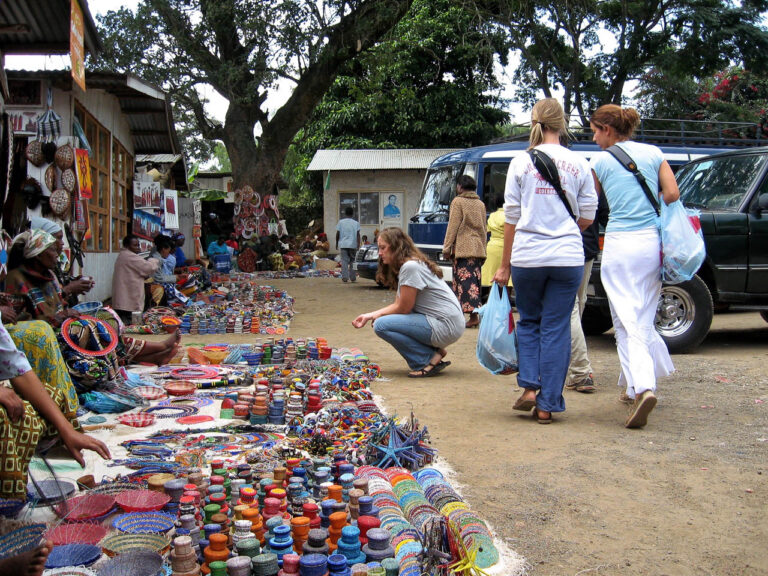 markt in Arusha met allerlei voorwerpen ,manden, kettingen halsbanden met drie toeristen die er langslopen