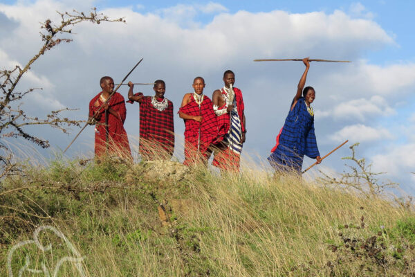 vijf masai mensen met speren bovenop een heuveltje