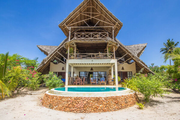 net op het strand een rond zwembad en villa gebouwd met houten palen een schuin rieten dak met drie verdiepingen tussen het groen op Zanzibar