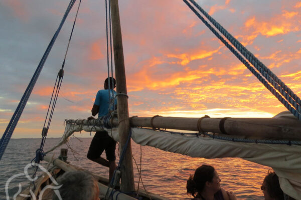 originele dhow, vissersboot, met mast waar man tegenaan staat en mensen in de boot voor een sunset cruise mafia eiland