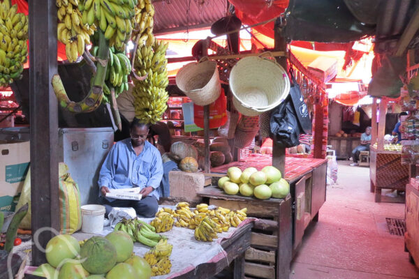 verse meloenen, bananen en manden met zittende lezende man op de Darjani markt Stone Town zanzibar