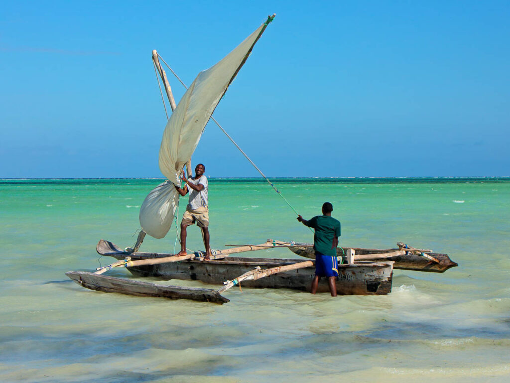 twee mensen op een smalle vissersboot met aan de zijkanten houten flappen voor de stabiliteit bij het strand van pangani tanzania