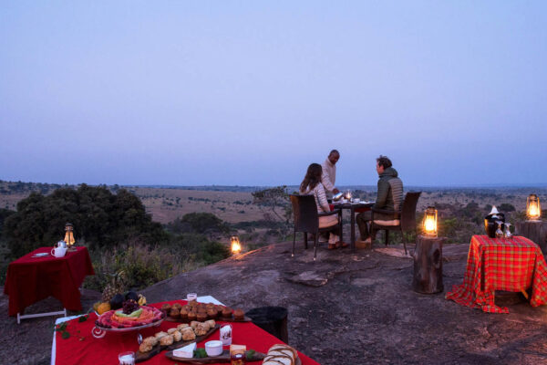 tafel met ontbijt en stel aan een tafel die bediend worden met uitzicht over de wakker wordende serengeti