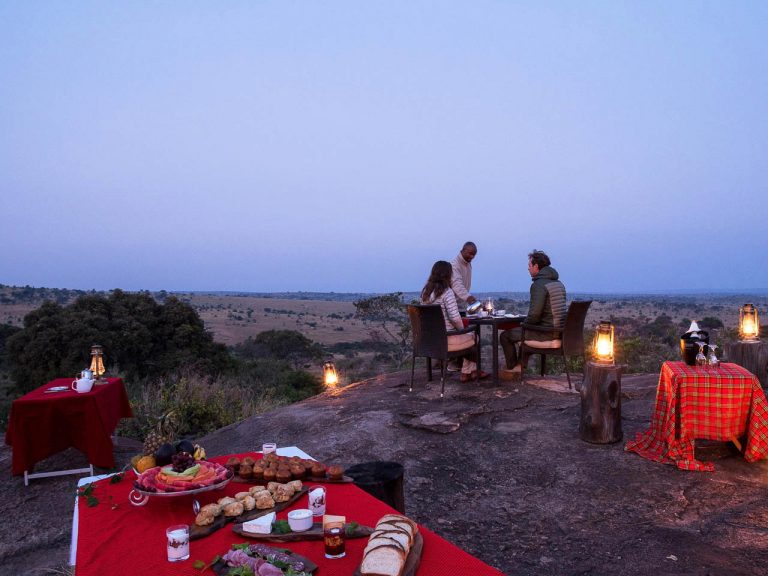 tafel met ontbijt en stel aan een tafel die bediend worden met uitzicht over de wakker wordende serengeti