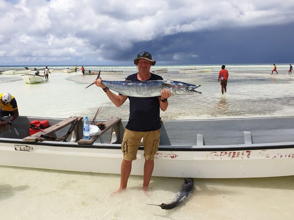 overzicht van een man met grote vis in zijn handen staand voor een bootje aan de zee zanzibar