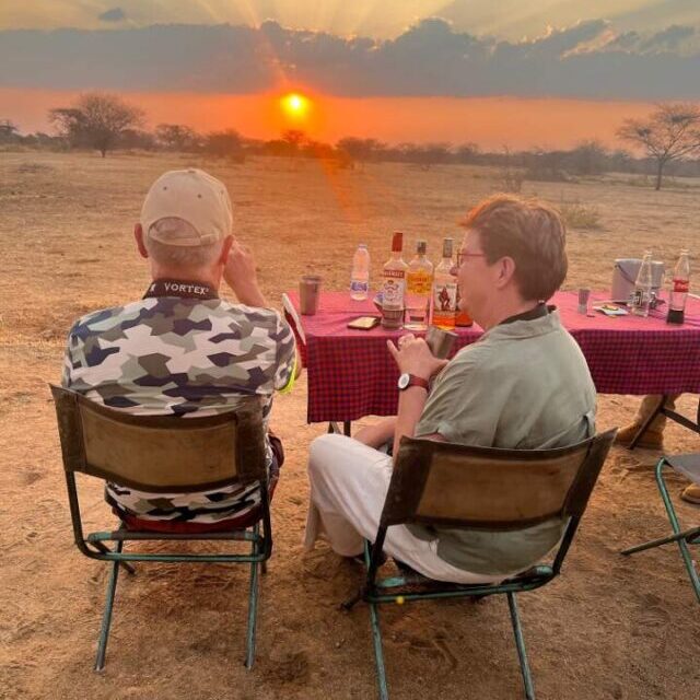 zittende man en vrouw tijdens een sundowner met een lekker drankje en een ondergaande zon in Ruaha national park tanzania
