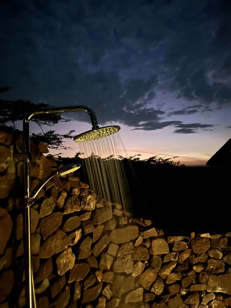 buitendouche bij lahia tented camp op de serengeti. de douche is ommuurt uit losse stenen en je hebt uitzicht over de serengeti