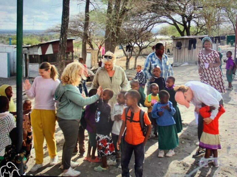 Culturele activiteit rondreis Tanzania. Gasten en lokale kinderen maken plezier en praten met elkaar tijdens een terug naar Tanzania reis