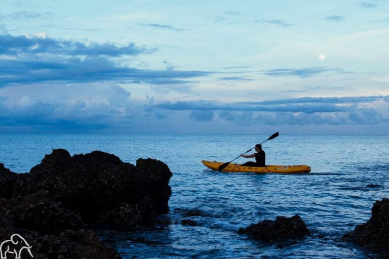 Kayakkende man op de Indische Oceaan met rotsblokken op de voorgrond en een mooie wolkenlucht erachter