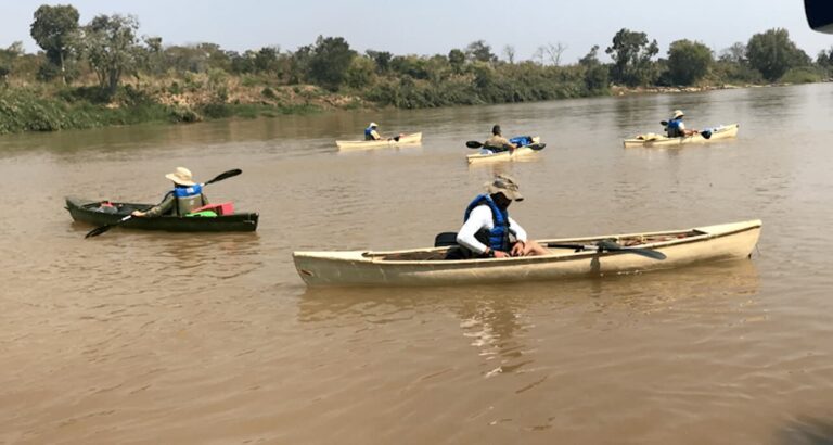 vier mensen in vier kano's op een rivier met bruin water