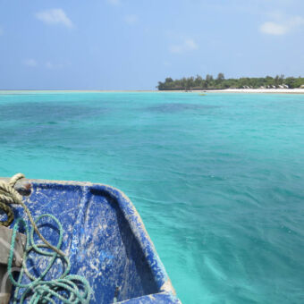 azuurblauwe oceaan vanaf een bootje zicht op een azuurblauwe zee en strand met groen en een staalblauwe lucht