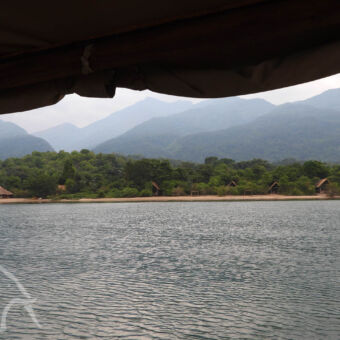 vanaf het water varend op de dhow een overzicht over het water naar een lodge in Tanzania bij Lake Tanganyika