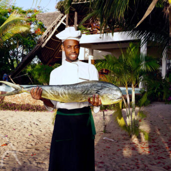 vis van de dag Kok staand met grote vis in beide handen staand voor een accomodatie op Zanzibar vis van de dag