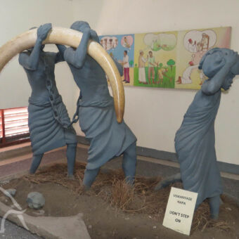 national museum In het national museum in Dar-es-Salaam twee beelden van geketende mensen die een slagtand op hun schouders dragen met daarvoor een kind met iets zwaars op zijn hoofd