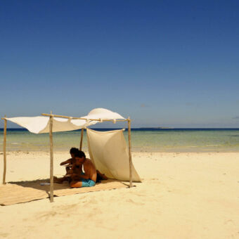 beach life op het strand twee mensen zittend onder een een lijfel bestaande uit vier houten palen met daartussen een doek gespannen uitkijkend over de indische oceaan op Fanjove eiland Tanzania