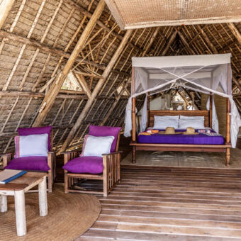banda binnen in een huisje in de vorm van een driehoek waarvan het dak bestaat uit balken en palmtakken met twee fauteuils met daarachter een groot bed met klamboe op Fanjove eiland genomen tijdens een huwelijksreis door Tanzania