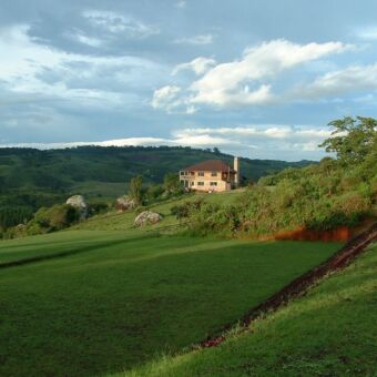 Mufindi highland lodge uitzicht vanaf een heuvel op Mufindi highland lodge een twee gebouw met verdiepingen midden in een heuvelachtig zeer groen landschap met grasland en bos