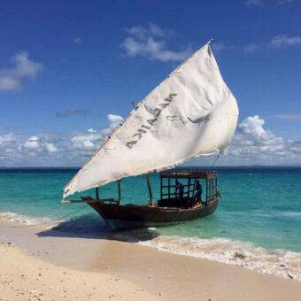dhow dhow aan de kust half op het strand met zeil en twee mensen op de boot bij Pangani