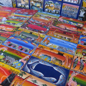 tinga-tinga schilderijen kleine rechthoekige schilderijen naast elkaar op de grond met kleurrijke afbeeldingen van dieren en mensen op simpel weergegeven dit wordt de tinga tinga schilderij genoemd