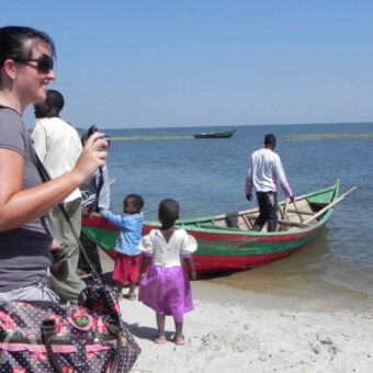 bezoek aan vissersdorpje vrouw met camera en twee kleine kinderen die bij een boot kijken met een man erin op lake victoria