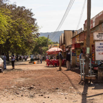 kapotte straat met wat bomen links en rechts oude huizen met golfplaten in Mto-wa-Mbu
