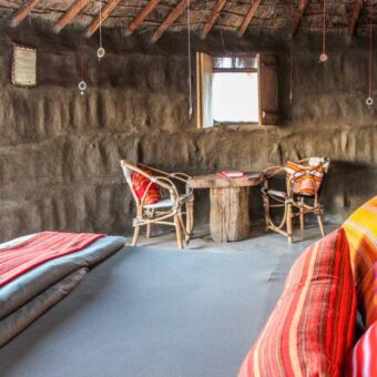 Twee persoons bed opgemaakt met felgekleurde oranje en rode kussens en plaids