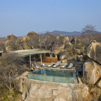 prachtig gelegen vierkant zwembad tussen kopjes / rotsen met ligstoelen en een vrouw die zwemt