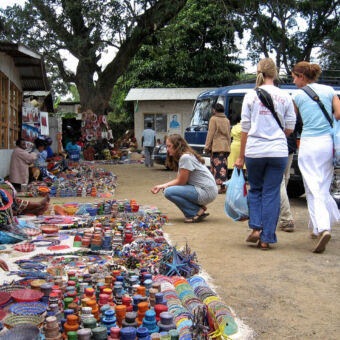 city tour Arusha markt in Arusha met allerlei voorwerpen ,manden, kettingen halsbanden met drie toeristen die er langslopen