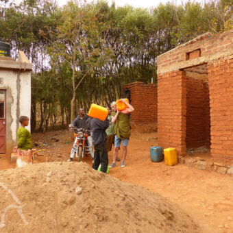helpen met het water op een excursie in de buurt van karatu een toerist met een cherry can op z'n schouder samen met een tanzaniaan die ook een cherry can heeft een vrouw staat toe te kijken