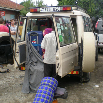 inpakken auto inpakken van de campingspullen in de safari auto door een man met een vrouw en kind links toekijkend