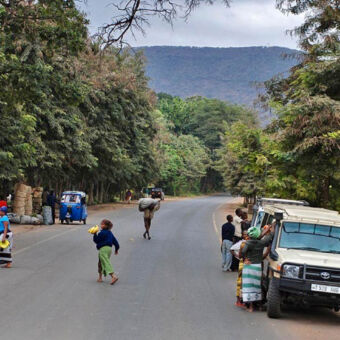 doorgaande weg doorgaande weg door dicht bebost gebied met vrouwen met bananen en safari auto rechts in Mto wa Mbu