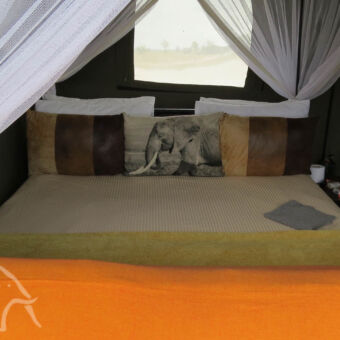 slapen in de bushrover bovenop een landrover is een plateau gemaakt waarop een tent staat en daarin zien we een bed met klamboe