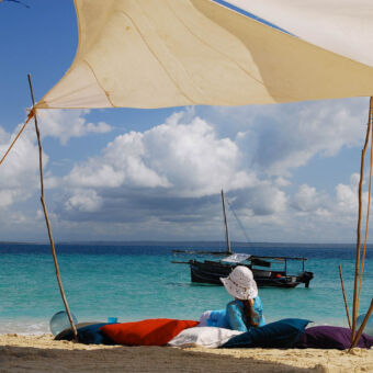 secret escape! vrouw liggend op een kleed onder dakje van tentdoek op een zandbank met een vissersboot op de achtergrond excursie vanuit pangani tanzania