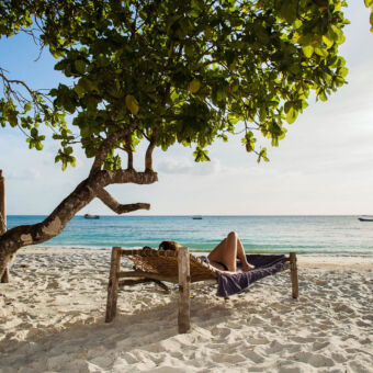 relaxen op het parelwitte strand zandstrand op pemba met een ligstoel met daarop iemand onder een boom aan de indische oceaan in tanzania