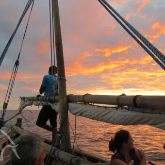 dhow sunset cruise originele dhow, vissersboot, met mast waar man tegenaan staat en mensen in de boot voor een sunset cruise mafia eiland