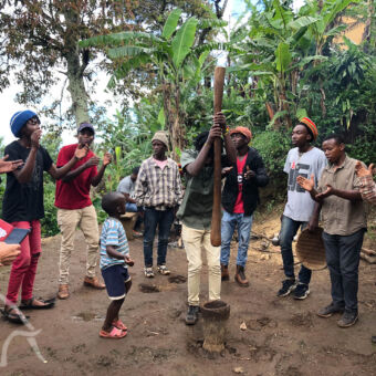 koffiebonen stampen klappende mannen in een kringetje met een man in het midden die met een grote houten stok koffie aan het stampen is in een kom