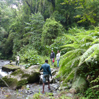door de rivierbedding drie mensen die op rotsen staan aan de oevers van een rivier kijkend naar mensen in de rivier vlakbij arusha tanzania