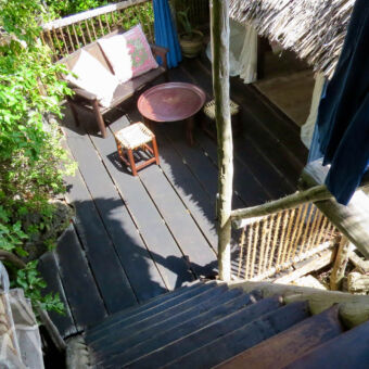 trap vanaf boven lopend naar beneden naar een boomhut met bietendak en veranda met bankje bij choke mjini treehouse mafia