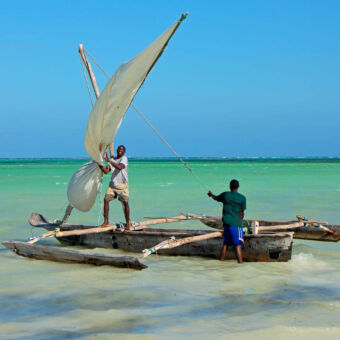 Tanzaniaanse dhow (kleine vissersboot) twee mensen op een smalle vissersboot met aan de zijkanten houten flappen voor de stabiliteit bij het strand van pangani tanzania