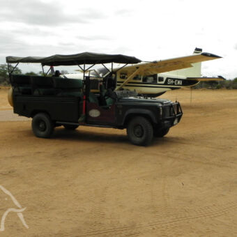 safari auto op de airstrip airstroip met sopen safari auto op de voorgrond en daarachter een net aangekomen klein vliegtuigje bij katavi