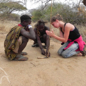 leren vuur maken jong meisje dat probeert samen met twee mannen van de hadzabe stam vuur te maken met een stokje