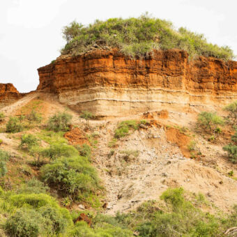 laagstructuur olduvai rots in tanzania met op de top gras daarna rood zandsteen overgaand in geel zandsteen uitstekend op een heuvel