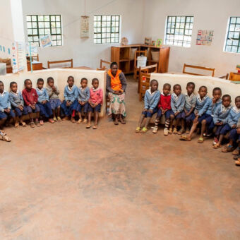 children home veel kleine weeskinderen zittend in een rondje met een vrouw in het midden in een stenen gebouw bij rhotia valley