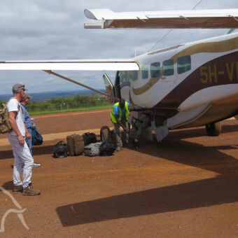 inpakken koffers in het laadruim twee mannen staand onder een vliegtuigvleugel naast het vliegtui wachtend op hun bagage met iemand die de bagage uit de buik haalt op en airstrip in tanznaia