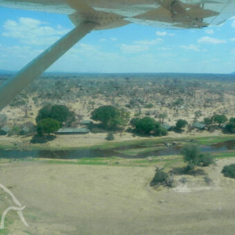 Ruaha van boven we zitten in een klein vliegtuigje en we zien nog net een klein stukje van de vleugel verderop zien we een lodge aan de Ruaha rivier