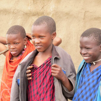 drie lachende en onderzoekende maaikinderen tijdens een rondreis door tanzania