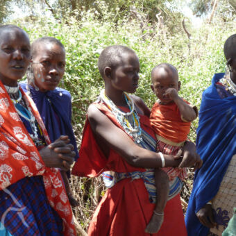 masai vrouwen met traditionele felgekleurde rode en blauwe kleding en een baby op de arm