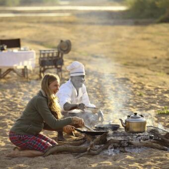 koken op de mooiste plekjes zittende vrouw met kok bij kampvuur tijdens fly camping kickaka meerdaagse luxe wandelsafari ruaha tanzania