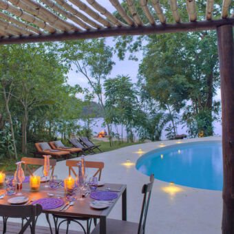 Rubondo Island Camp private dining tafel mooi gedekt met kaarsjes aan het zwembad voor een privé diner met op de achtergrond een kampvuur en lake victoria rubondo romantisch huwelijksreis